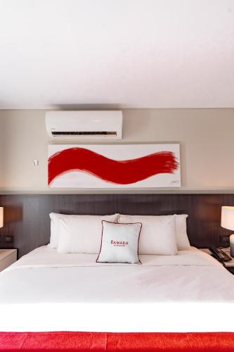 a bedroom with a white bed with a red painting above it at Ramada Suites by Wyndham Asuncion Aeropuerto in Asuncion