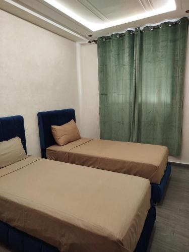 two beds in a room with green curtains at Le refuge de Vittel 3 in Ifrane