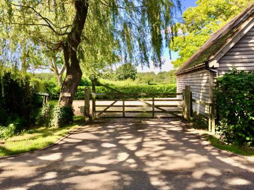 a wooden fence next to a tree and a house at Luxurious Country Barn in Baughurst