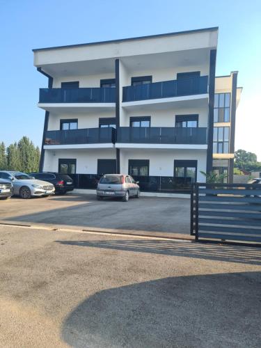 a building with cars parked in a parking lot at Nejla Apartmani Stoj in Ulcinj