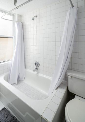 a white bathroom with a tub and a toilet at Bright 1BR Escape in Lower East Side NYC in New York