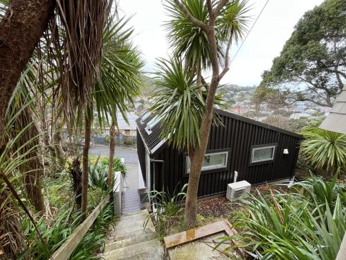 a black house with palm trees in front of it at Cosy, new, quiet Island Bay studio in Wellington
