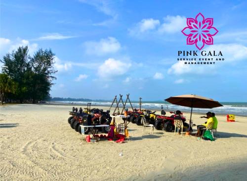 a group of people sitting under an umbrella on a beach at Timurbay Sidecation Studio - Walk to Beach, Enjoy Pool & Sea View by PG Management in Kampung Saberang Balok