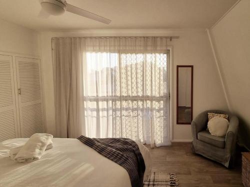 a bedroom with a bed and a chair and a window at Central Bargara Beach Bungalow by UG in Bargara
