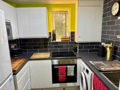 a kitchen with white cabinets and black tiles at Hathaway guest room in Greenford