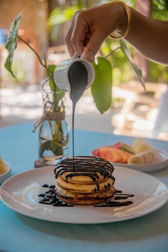 a person pouring syrup onto a stack of pancakes on a plate at Villa Tahid in Gili Air