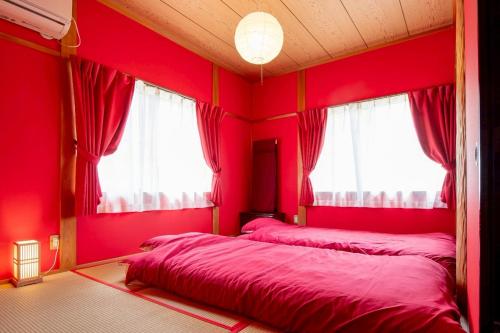 two beds in a room with red walls and windows at Nagata House in Ise