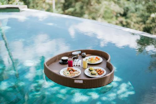 een dienblad met eten op een tafel in een zwembad bij Umah Bali Kuno Villa in Tampaksiring