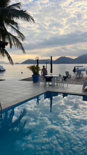 a man sitting at a table next to a swimming pool at EXCLUSIVIDADE à beira-mar in Angra dos Reis