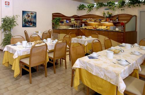 a dining room with tables and chairs and a kitchen at Aparthotel Pineda in Bibione