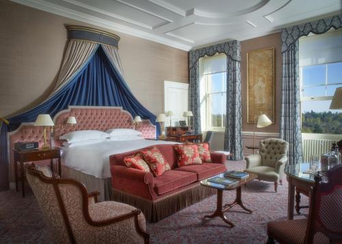 a bedroom with a large bed and a red couch at Cliveden House - an Iconic Luxury Hotel in Taplow