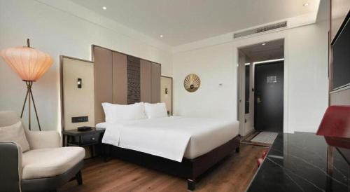 a bedroom with a white bed and a chair and a desk at Jinjiang Metropolo Haikou East High Speed Railway Station Normal University in Haikou
