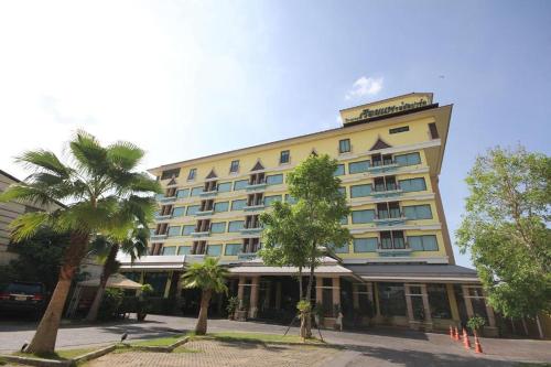 a large yellow building with palm trees in front of it at Ruean Phae Royal Park Hotel in Phitsanulok