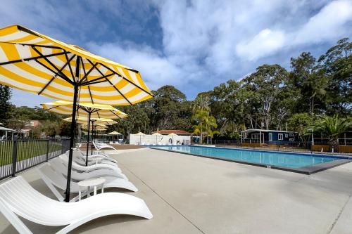 a group of chairs with umbrellas next to a swimming pool at Tasman Holiday Parks - Kioloa Beach in Kioloa