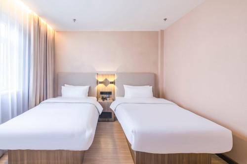 two beds in a hotel room with white sheets at Hanting Hotel Beijing Daxing Caiyu in Beijing