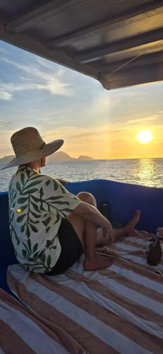 a person in a hat sitting on a boat watching the sunset at Balai Adlao in El Nido