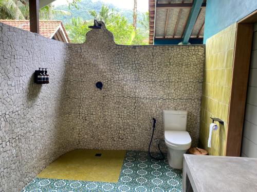 a bathroom with a toilet and a tiled wall at Darmada Eco Resort in Sidemen