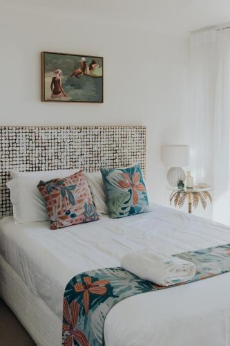 a white bed with pillows and a picture on the wall at Pandanus Palms Holiday Resort in Point Lookout