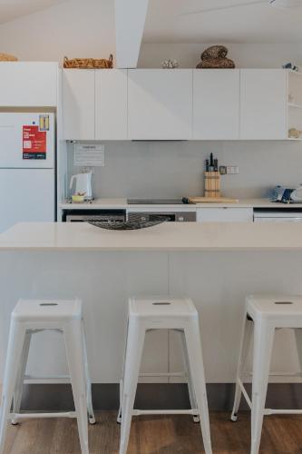 a kitchen with white cabinets and two white stools at Pandanus Palms Holiday Resort in Point Lookout