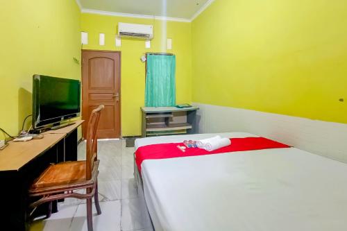a room with a bed and a desk and a television at WILUDJENG Guest House near Alun Alun Sragen Mitra RedDoorz in Sragen