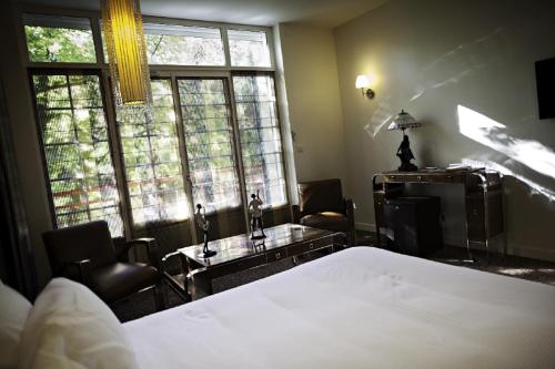 a bedroom with a bed and a desk and windows at Demeures & Châteaux La Belle Meuniere in Royat