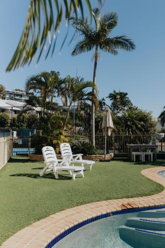 two white chairs sitting next to a swimming pool at Pandanus Palms Holiday Resort in Point Lookout