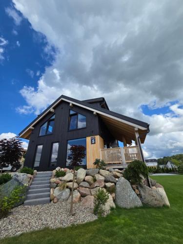 a black house with rocks in front of it at Czôrny Dąb - nowoczesny dom wakacyjny na Kaszubach, jacuzzi, sauna, bilard in Garcz