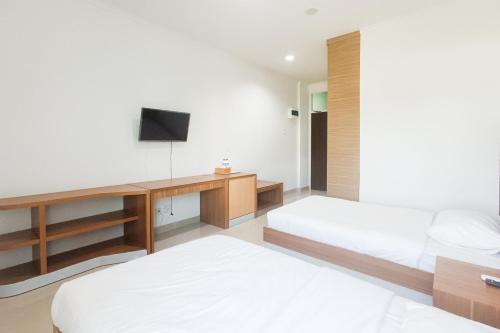 a bedroom with two beds and a desk with a television at Urbanview Hotel Syariah UIN Mataram in Mataram