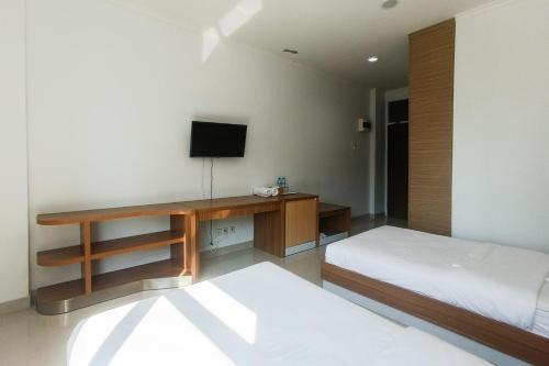 a bedroom with two beds and a desk with a television at Urbanview Hotel Syariah UIN Mataram in Mataram