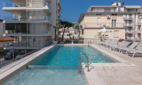 a swimming pool with chairs and a building at Hotel Jesulum in Lido di Jesolo