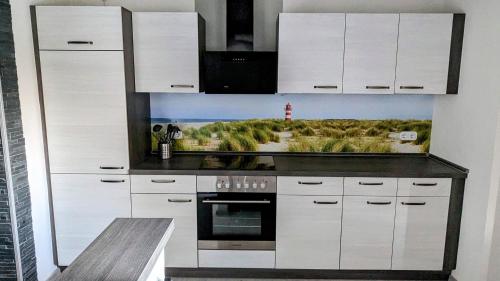 Una cocina con gabinetes blancos y un cuadro en la pared. en Ferienhaus Meer & Mehr, en Wilhelmshaven