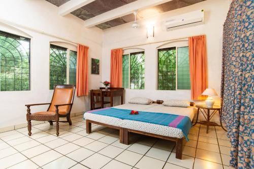 a bedroom with a bed and a chair and windows at Gaia's Garden Guest House in Auroville