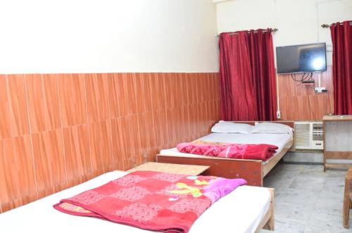 two beds in a room with red curtains and a tv at HOTEL SAVITRI Nearest Deoghar Mandir in Deoghar