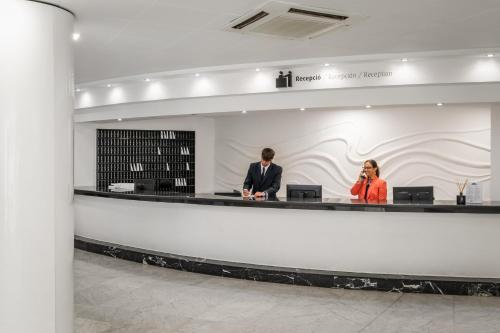 a man and a woman standing at a counter in a lobby at Hotel Mercury by ALEGRIA in Santa Susanna