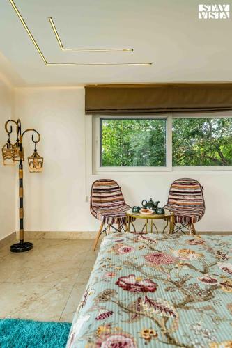 a bedroom with two chairs and a table and two windows at StayVista at Kuber Vatika with BBQ & Bonfire in Jaipur