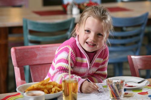 a little girl sitting at a table with a plate of food at Hasseröder Ferienpark in Wernigerode