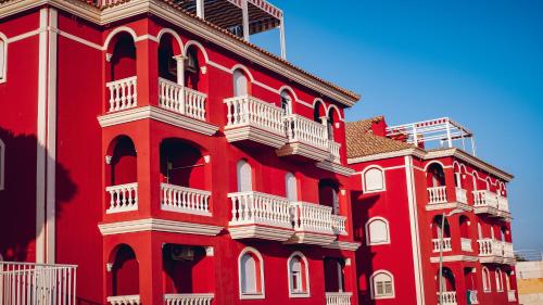 a red building with white balconies on the side of it at Apartamento rojo con vistas al mar in Mazagón