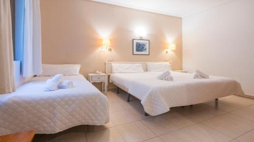 two beds in a hotel room with white sheets at Hostal Centro in Toledo