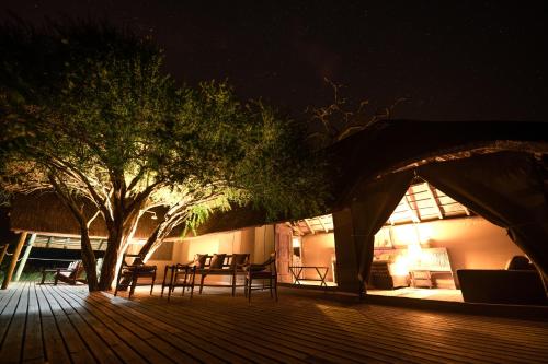 a wooden deck with chairs and a tree at night at South Okavango - Omogolo Hideaways in Rammu