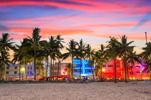 a beach with palm trees and buildings at sunset at Heart of Ocean Drive - Studio - Rooftop Pool in Miami Beach