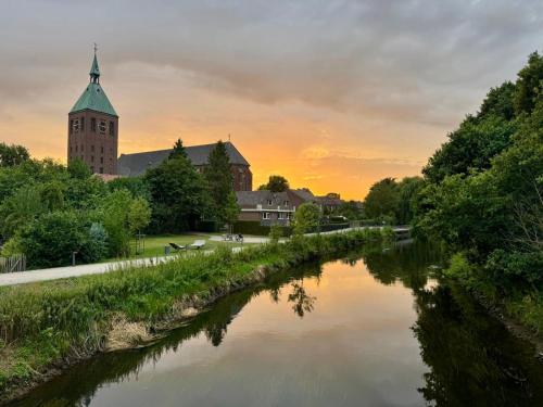 a river with a church and a clock tower at Ferienhaus an der Niers in Weeze