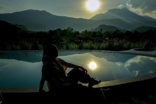 a person sitting next to a pool of water with the sunset at Mật Retreat in Ba Vì
