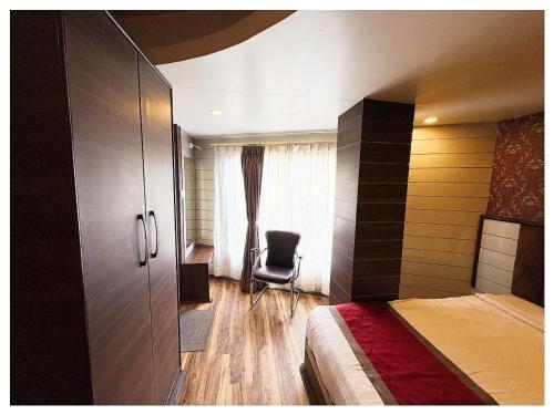 a bedroom with a bed and a chair next to a window at Hotel Zambala Retreat & Spa Darjeeling in Darjeeling