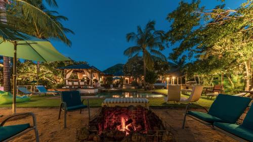 a fire pit in a yard with chairs and an umbrella at Shanti Ghar Guest House in Tamarin