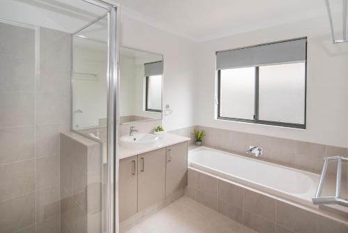 a bathroom with a tub and a sink and a mirror at Pearl Mews - Heart of Busselton in Busselton