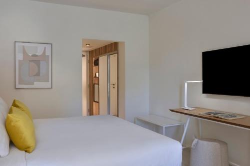 a white bedroom with a bed and a desk with a television at Atlantica Nissaki Beach - Adults Only in Gimari