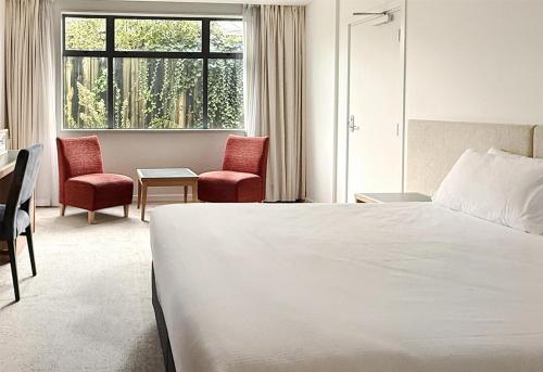 a bedroom with a bed and two chairs and a window at Sudima Hotel Lake Rotorua in Rotorua