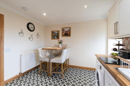 a kitchen with a table and chairs and a clock on the wall at Bungalow with Hot Tub, BBQ Hut, Golf Net , Large Garden & Play Area in Maybole