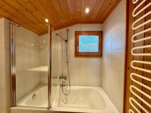 a bathroom with a tub with a shower and a window at Chalet Bliss with Spectacular Views in Chateau-d'Oex