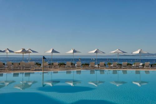 a swimming pool with umbrellas and chairs and the ocean at Atlantica Nissaki Beach - Adults Only in Gimari